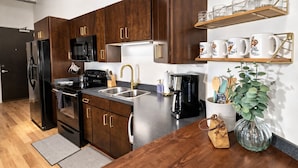 A modern kitchen with dark wood cabinets, stainless steel appliances, a black refrigerator, a microwave, a coffee maker, and a plant on the counter.