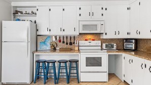 Cucina con pensili e basi bianche, forno a microonde, fornello e tostapane, con sgabelli da bar blu.
