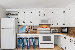 A kitchen with white cabinets, a microwave, a stove, a toaster, and blue bar stools.