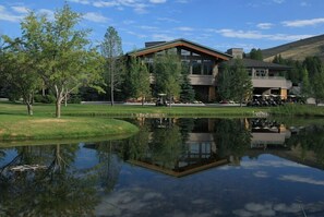 A modern building with a reflection in a pond, surrounded by trees and a grassy area.