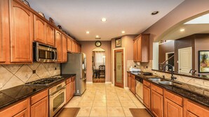 A modern kitchen with wooden cabinets, stainless steel appliances, and a tiled floor.