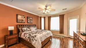 A bedroom with a wooden bed, a nightstand, a ceiling fan, and two wall-mounted artworks.