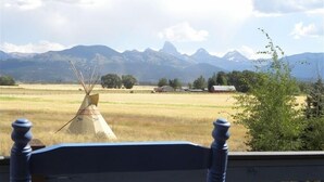 Vista desde un porche con banca de madera, con un paisaje rural que incluye un tipi tradicional, campos abiertos y montañas a lo lejos.