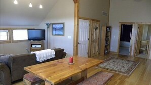 Un espacio habitable amplio con una mesa de comedor de madera, bancos, un sofá y un televisor.