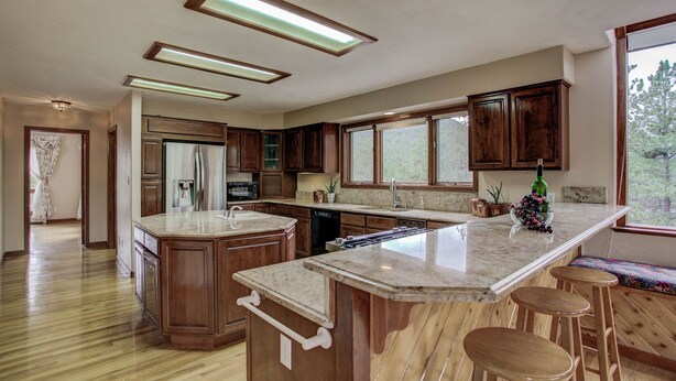 Une cuisine spacieuse avec des meubles en bois, un grand îlot central doté de tabourets et une vue sur l’extérieur grâce à de grandes fenêtres.