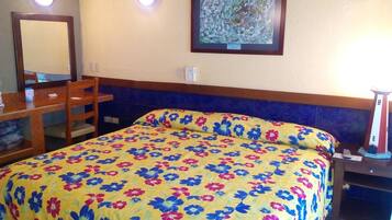 A hotel room with a bed, a desk, a chair, a mirror, and a nightstand.