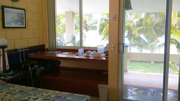 A room with a dining area, a window with a view of palm trees, and a door leading outside.