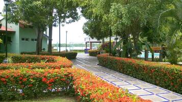 Un sendero bordeado por coloridas flores y árboles, que conduce a un edificio con techo azul.