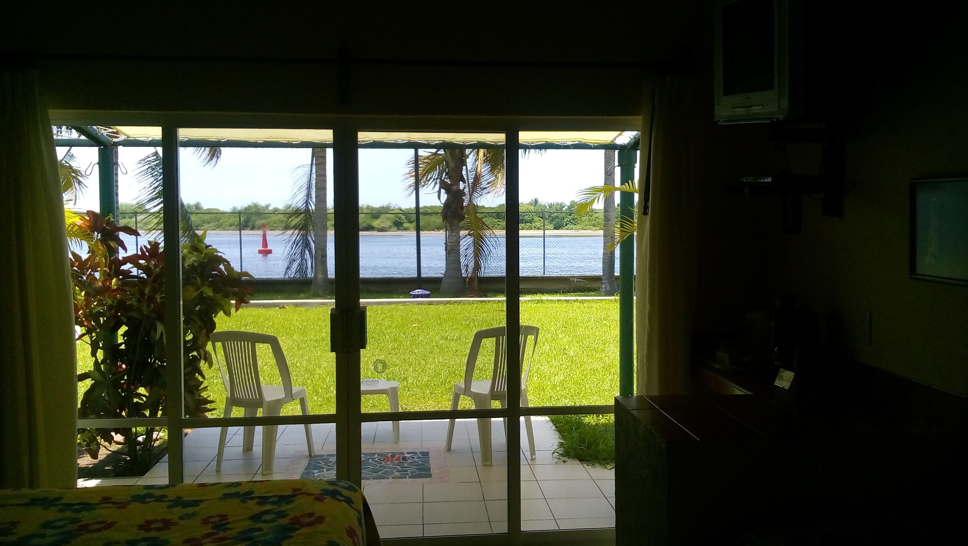 Una habitación con un amplio ventanal corredera que da a un balcón con vistas a un lago y palmeras.
