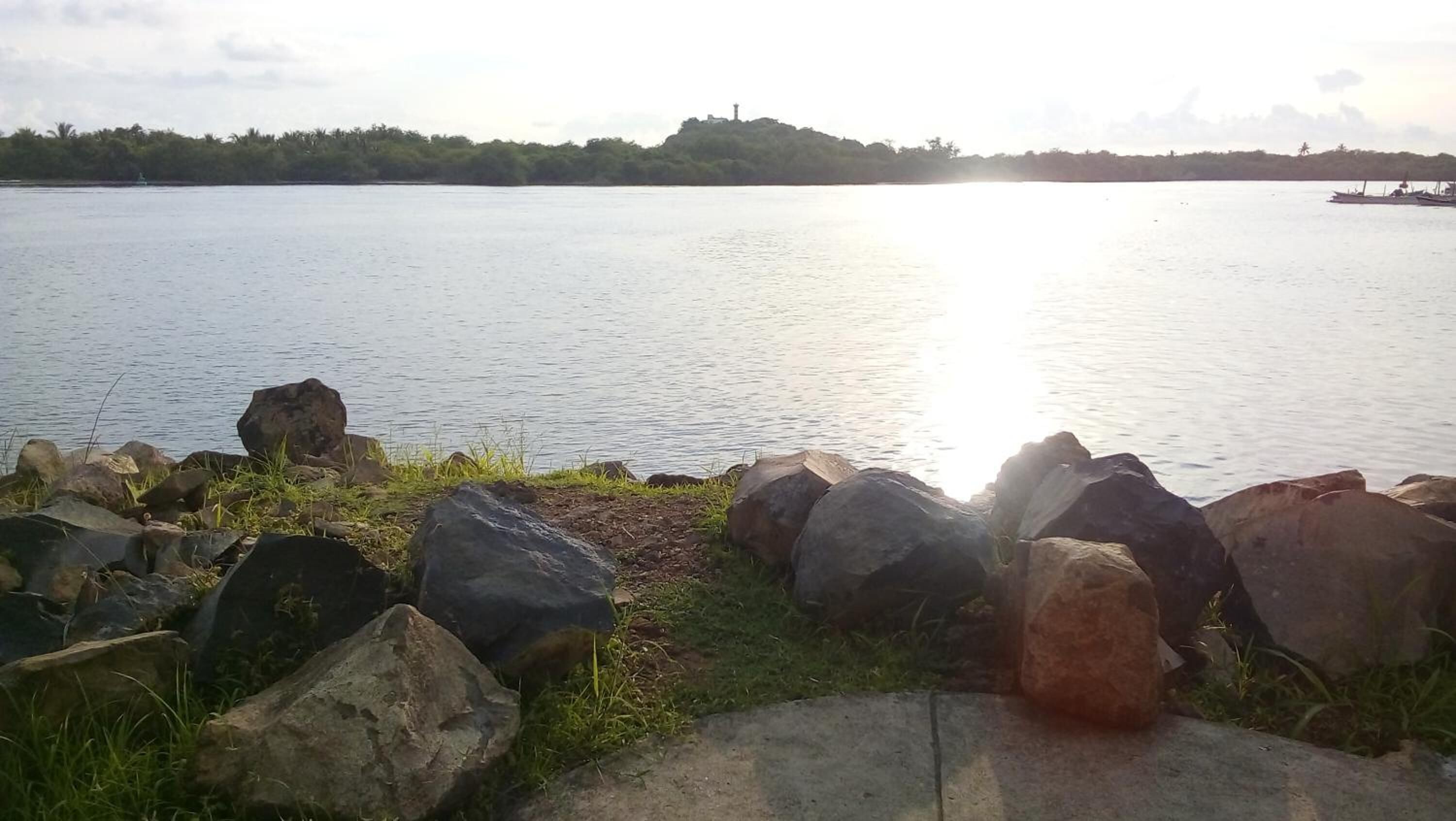 Um lago calmo com pedras grandes em primeiro plano e uma colina distante com uma construção no topo.