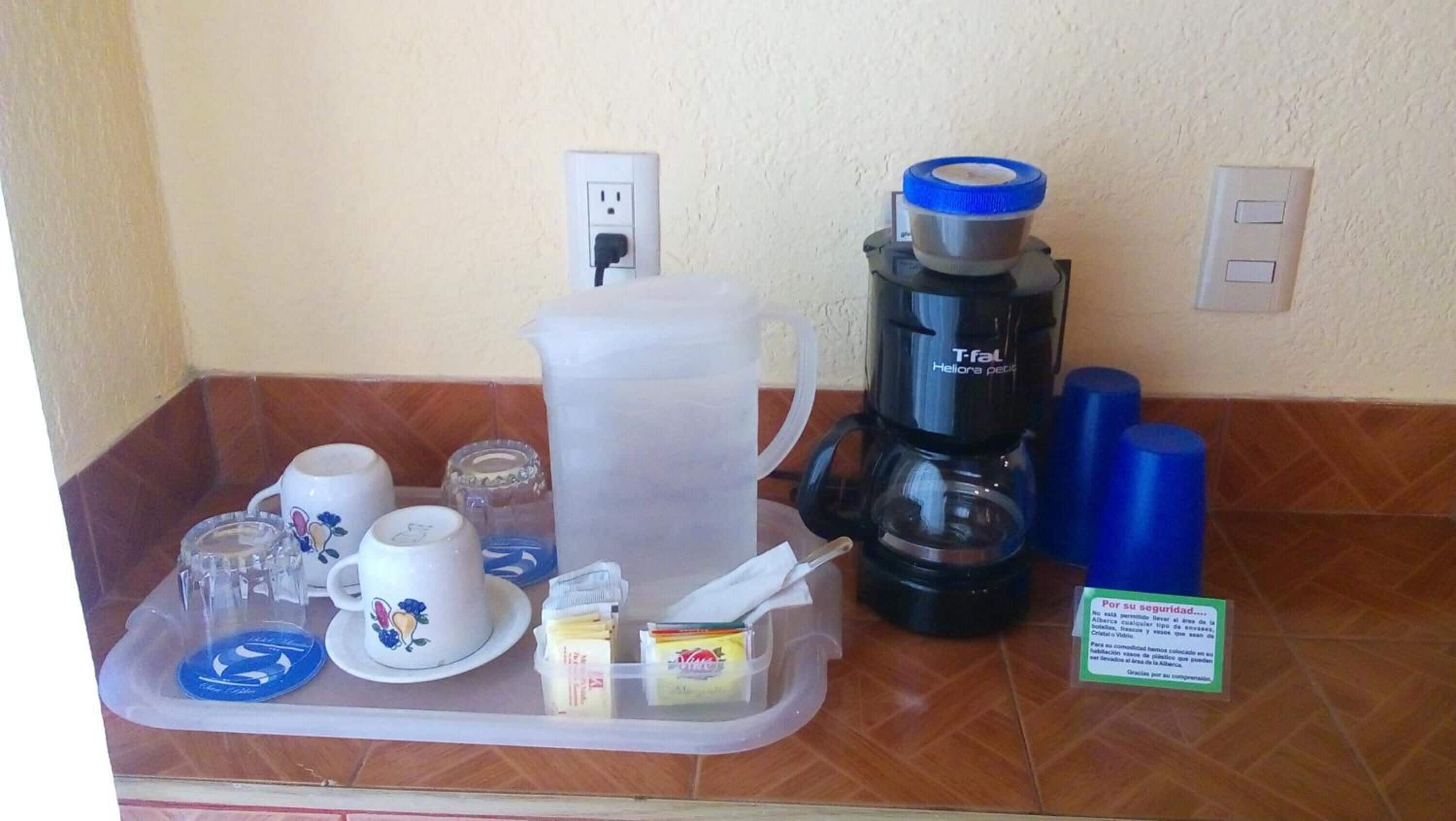 A breakfast tray with a coffee maker, cups, and a pitcher on a kitchen counter.