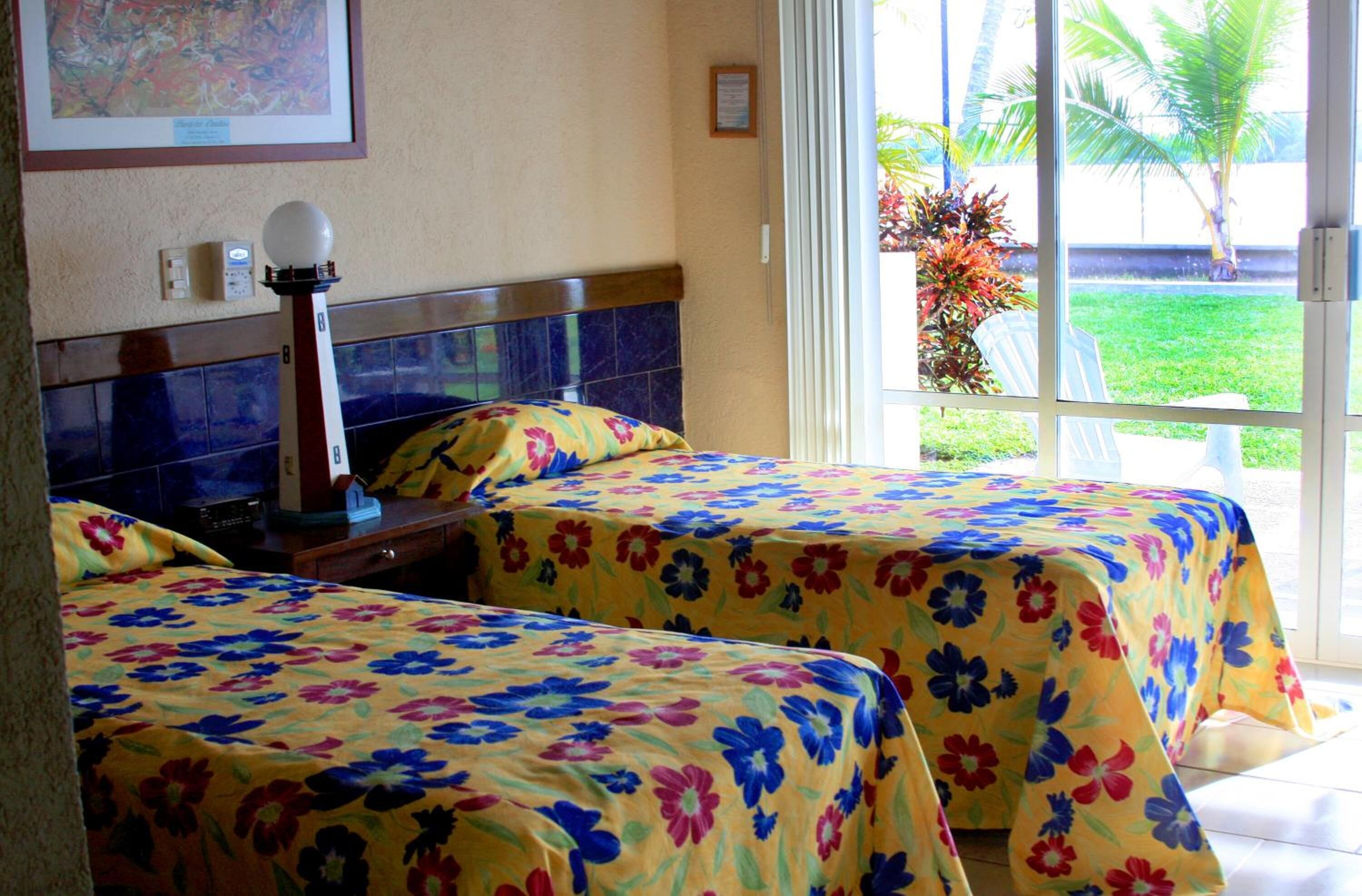 A hotel room with two beds, a nightstand, a lamp, a television, and a window with a view of the outdoors.