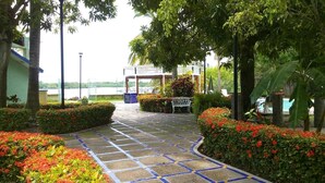 A paved pathway leading to a covered seating area surrounded by lush greenery and vibrant flowers.