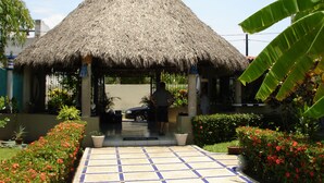 A thatched-roof structure with a tiled entrance, surrounded by potted plants and flowers.