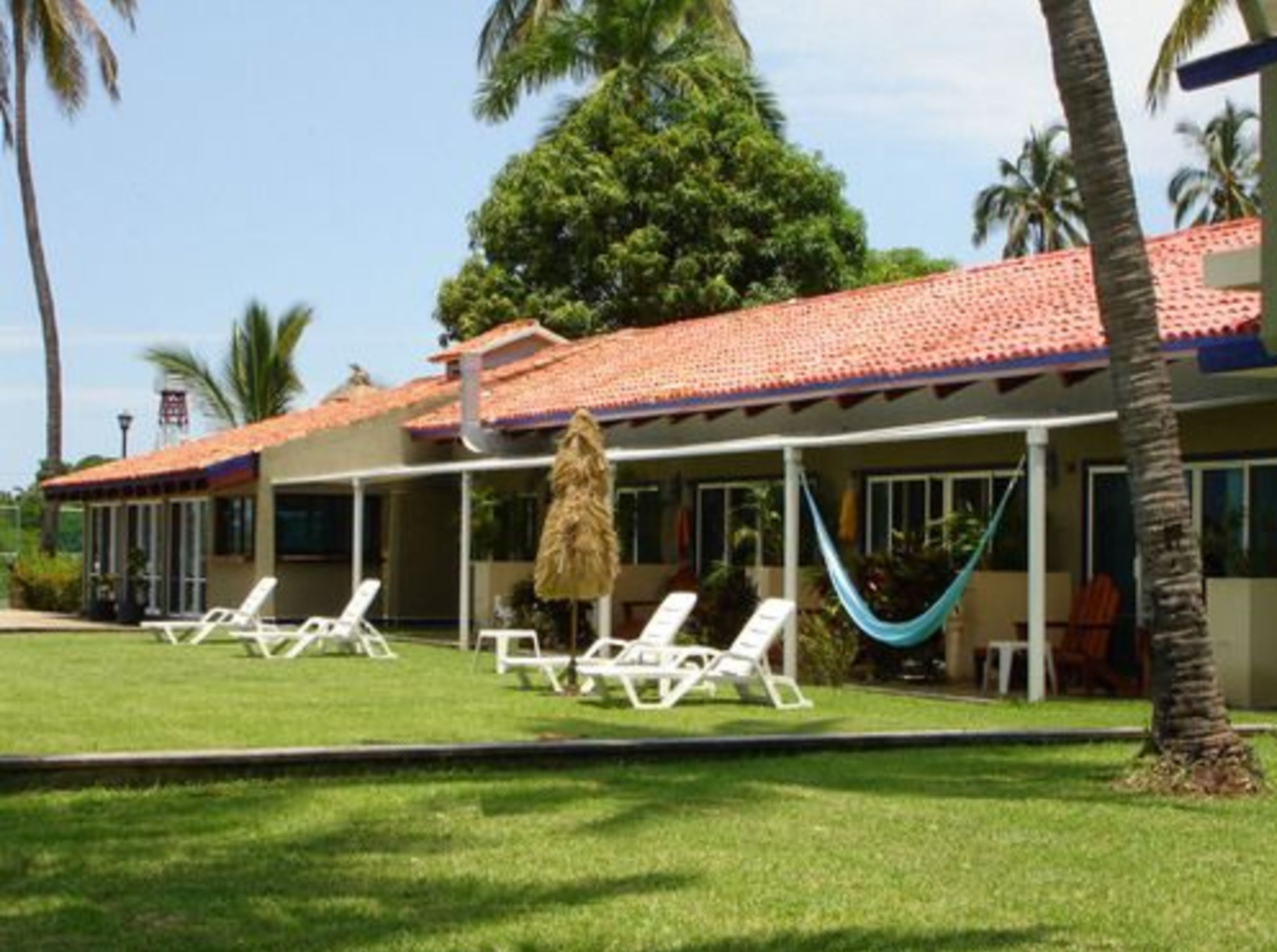 A hotel with a red-tiled roof, white lounge chairs, and a hammock.