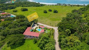 An aerial view of a green landscape with a red-roofed building, a swimming pool, and a road leading to the coast. - Beautiful Condominium - Wifi access throughout and 300 Yards from the Beach! (Samara)