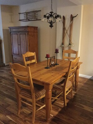 A wooden dining table with four chairs, a chandelier, and candles on the table.