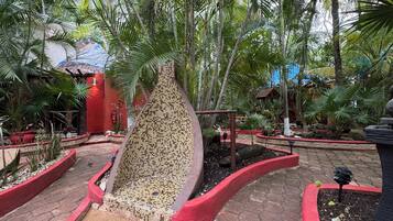 Un jardin tropical agrémenté d’une fontaine carrelée, de palmiers et de jardinières rouges.