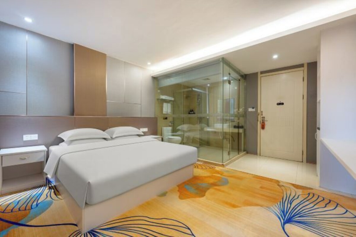 A modern bedroom with a bed, bedside table, and a glass-enclosed walk-in closet.