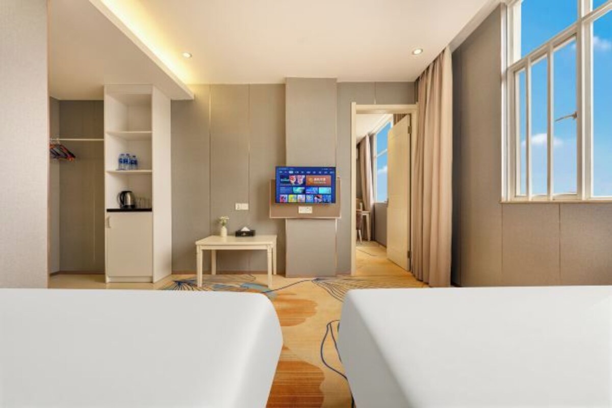 A hotel room with two beds, a TV, a desk, a wardrobe, and a window with a view.