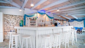 A bar area with a stone wall, white bar stools, and a variety of bottles. - Porto Koukla Beach Hotel (Zakynthos)