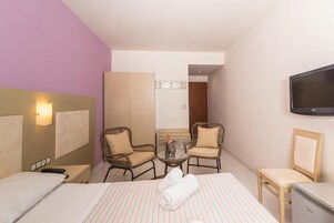 Una camera d'albergo con un letto, due sedie, un tavolino con una bottiglia e dei bicchieri, una televisione e un frigobar.