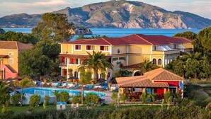 A hotel with a swimming pool, red-roofed buildings, and a view of the sea and mountains. - Porto Koukla Beach Hotel (Zakynthos)
