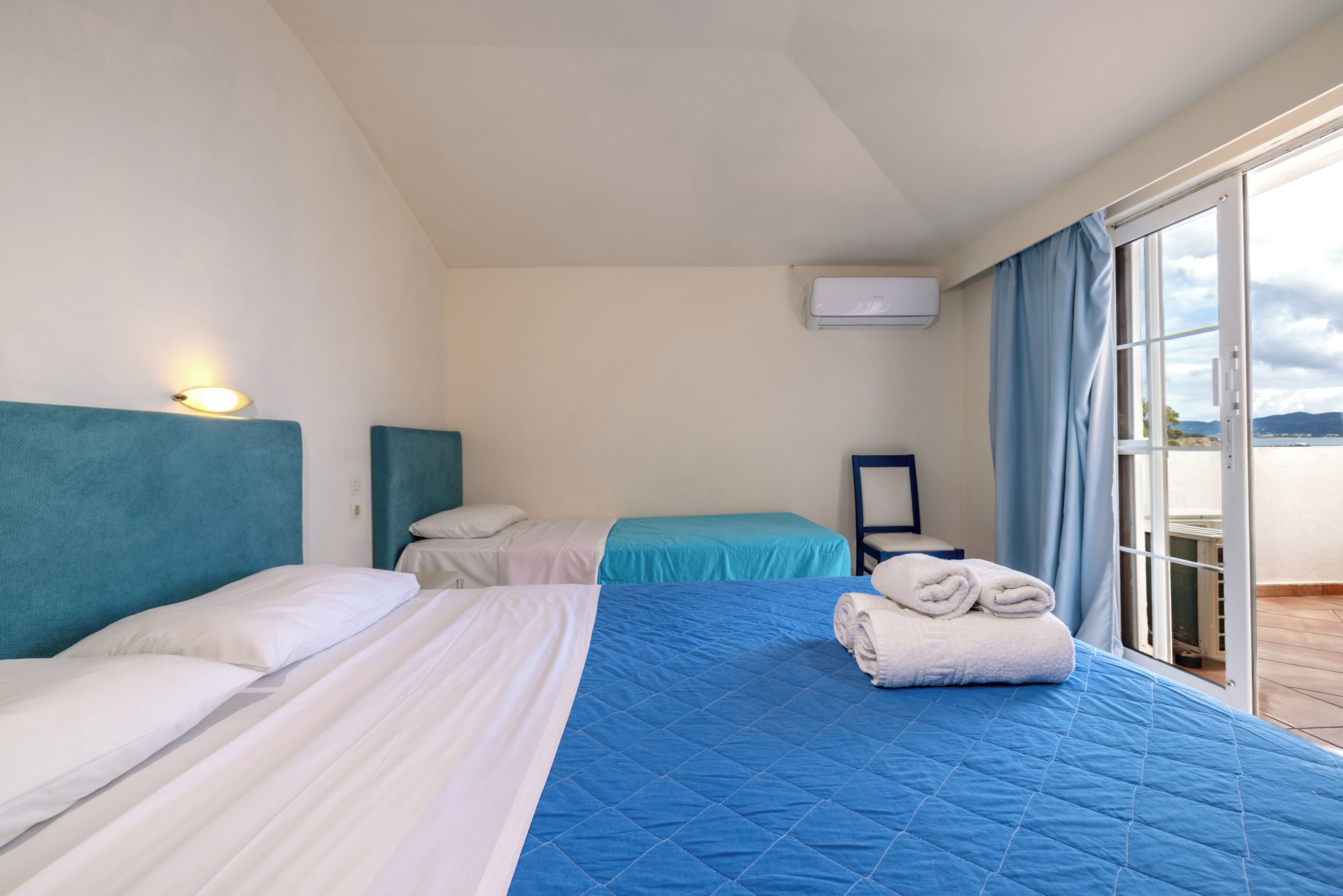Ett hotellrum med två sängar, ett stort fönster med gardiner, en luftkonditioneringsanläggning och utsikt över omgivningarna.