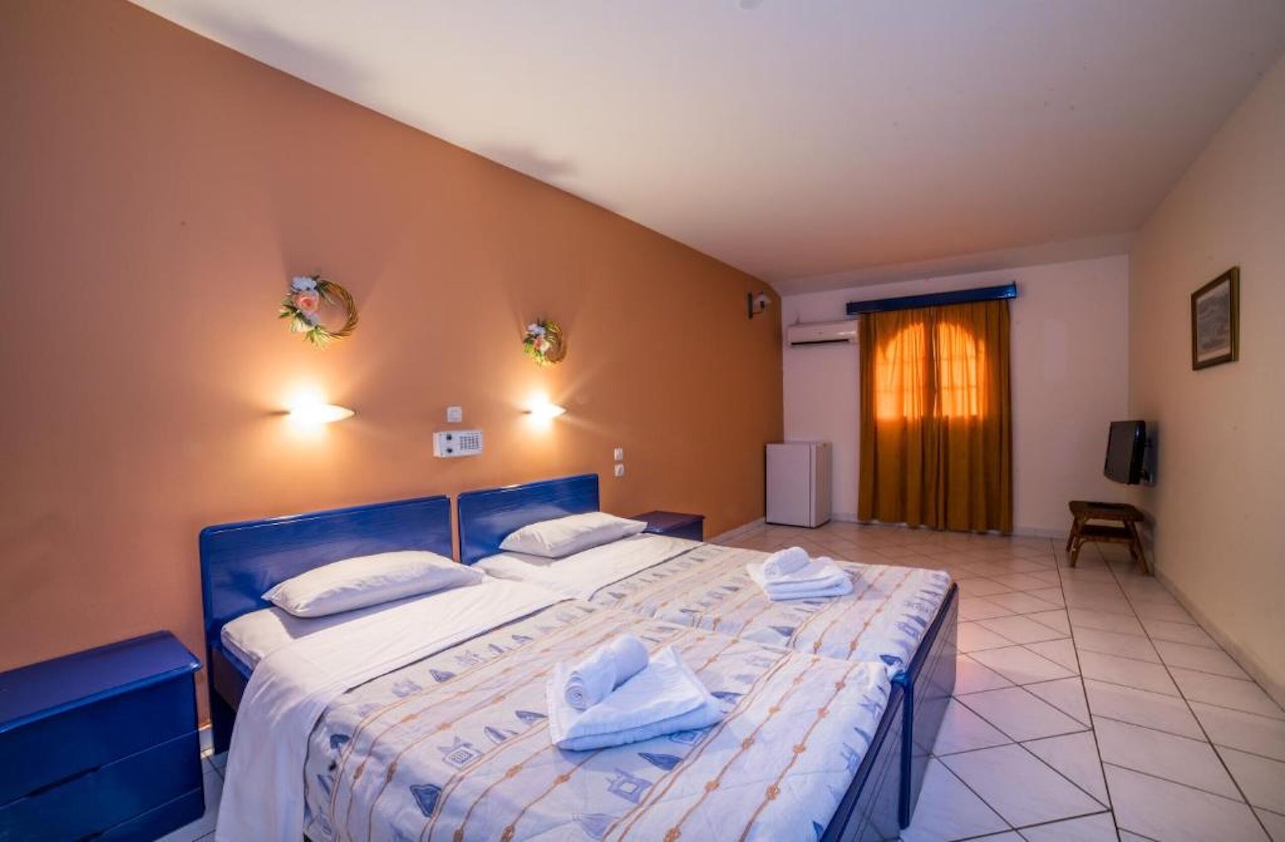 Habitació d'hotel amb un llit, dues làmpades penjades a la paret, un petit escalfador, una televisió i una porta amb cortines.