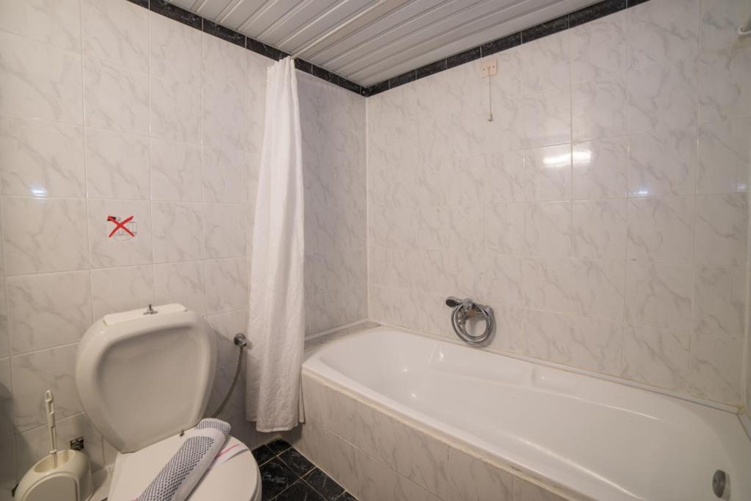A bathroom with a toilet, a shower curtain, and a bathtub.