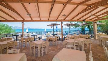 An outdoor patio with tables and chairs, a wooden ceiling, and a view of the sea.