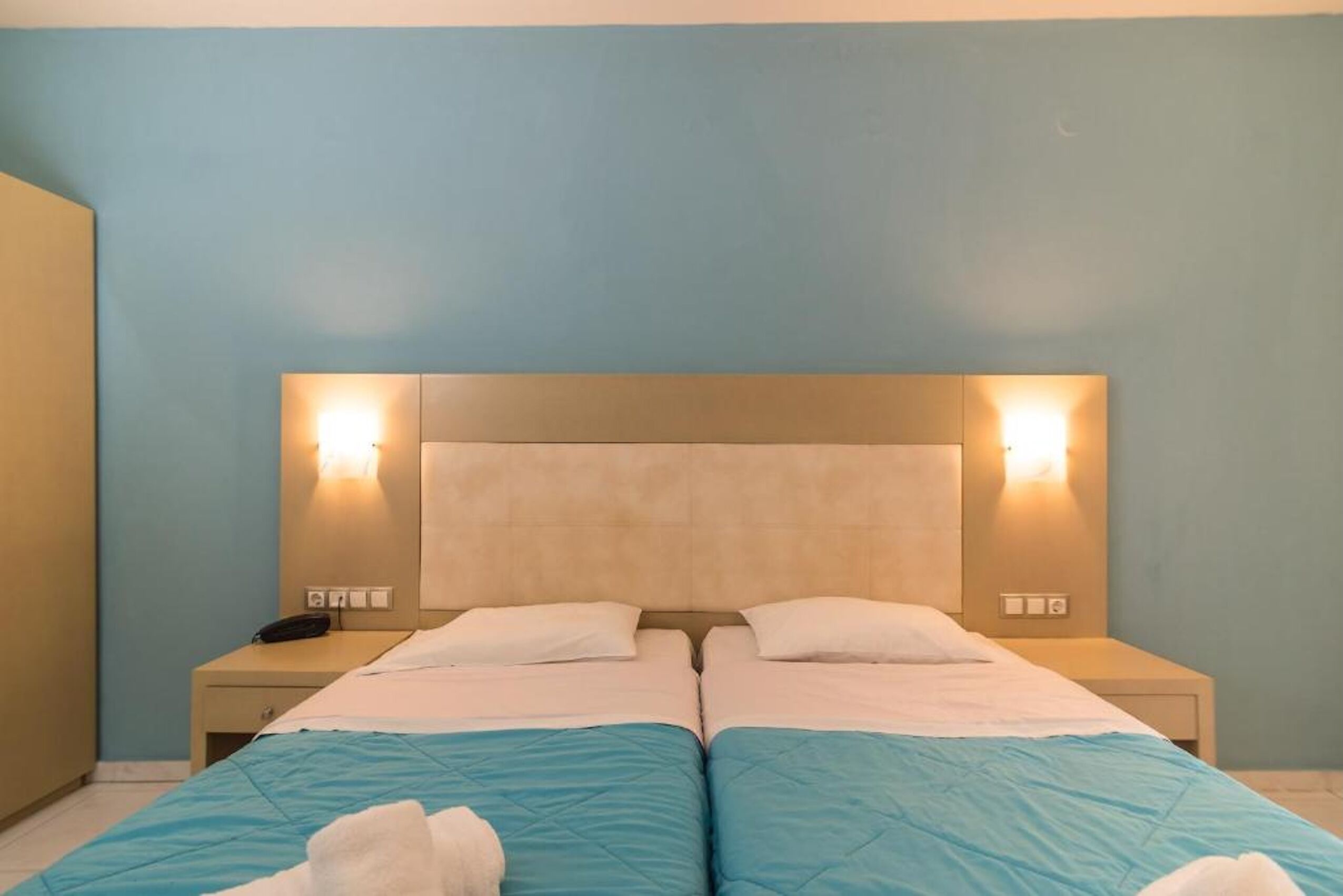 Habitación doble con dos camas, mesitas de noche e iluminación de pared.
