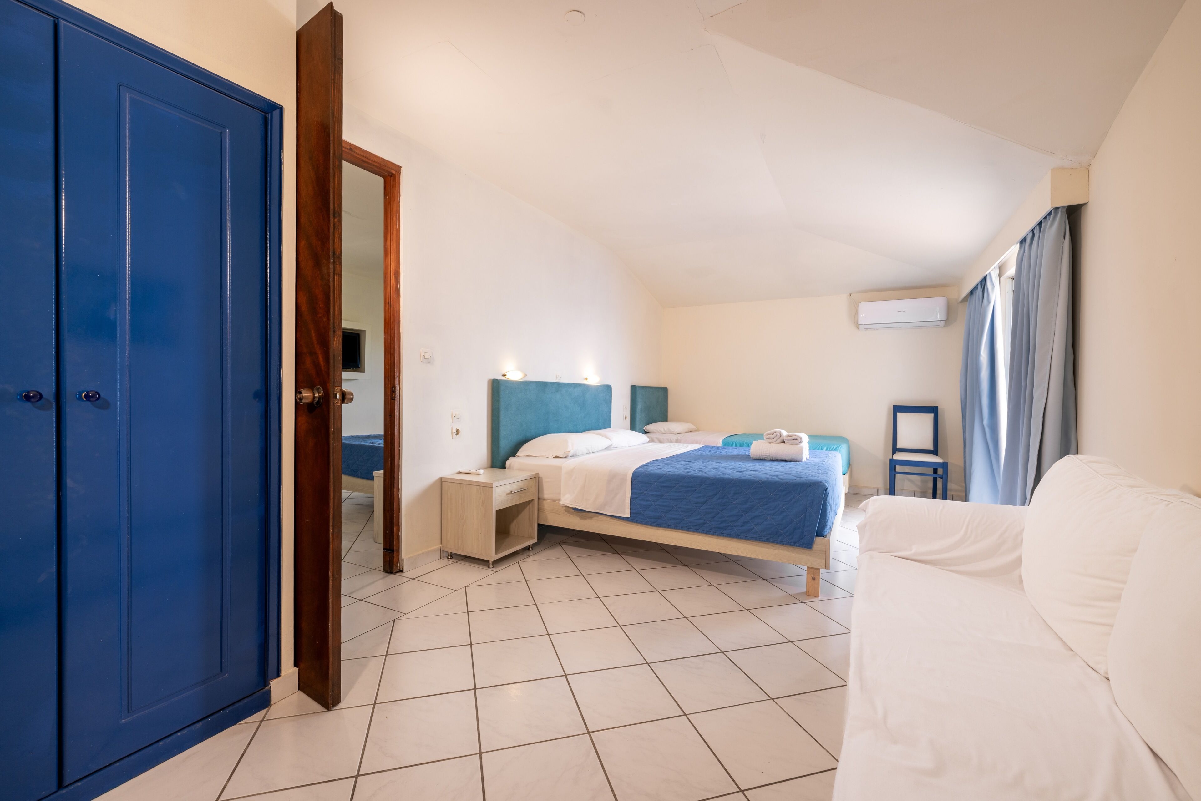 A bedroom with a bed, bedside tables, a wardrobe, a sofa, and an air conditioning unit.