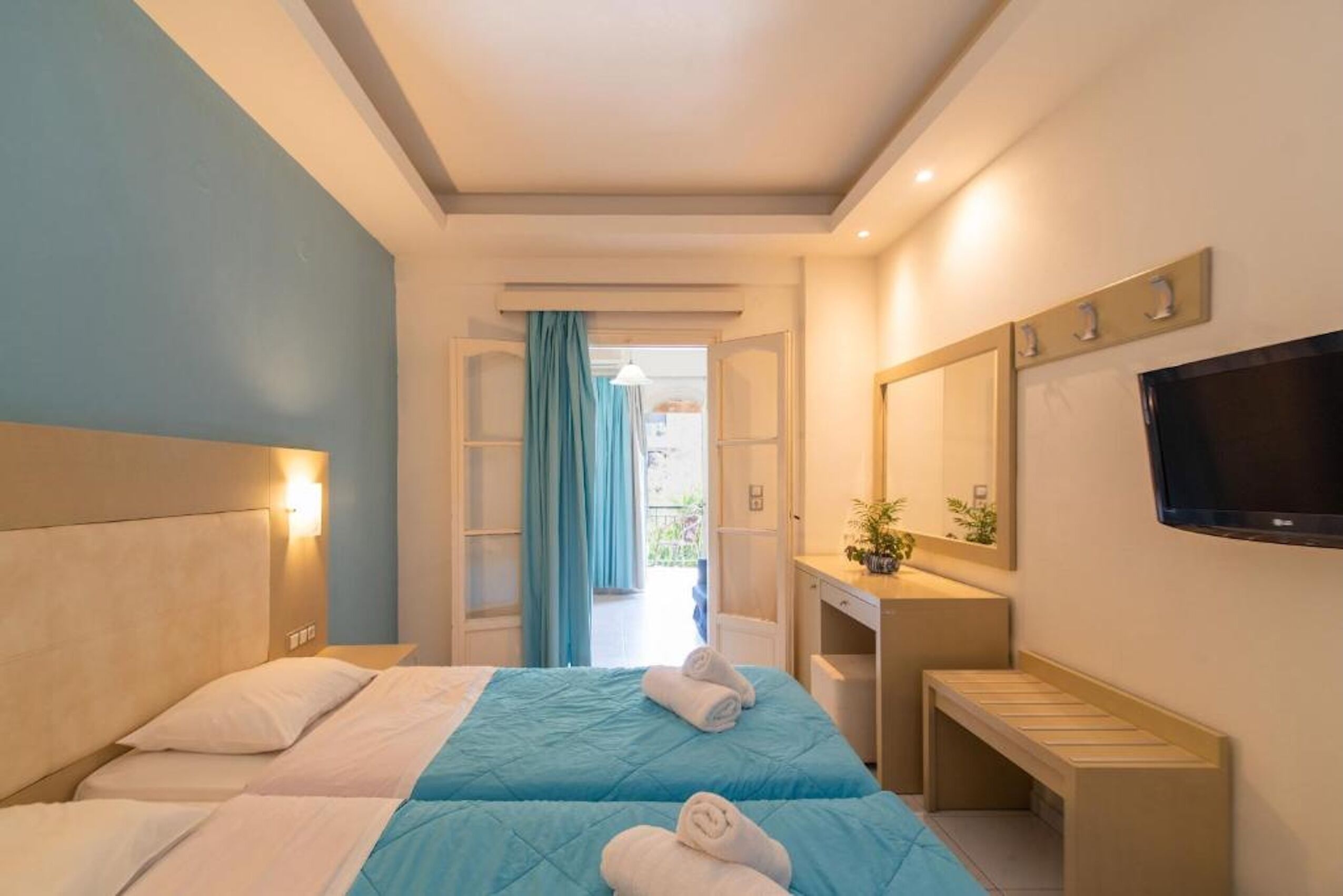Habitación de hotel con dos camas, un escritorio, un televisor y un baño visible a través de una puerta abierta.