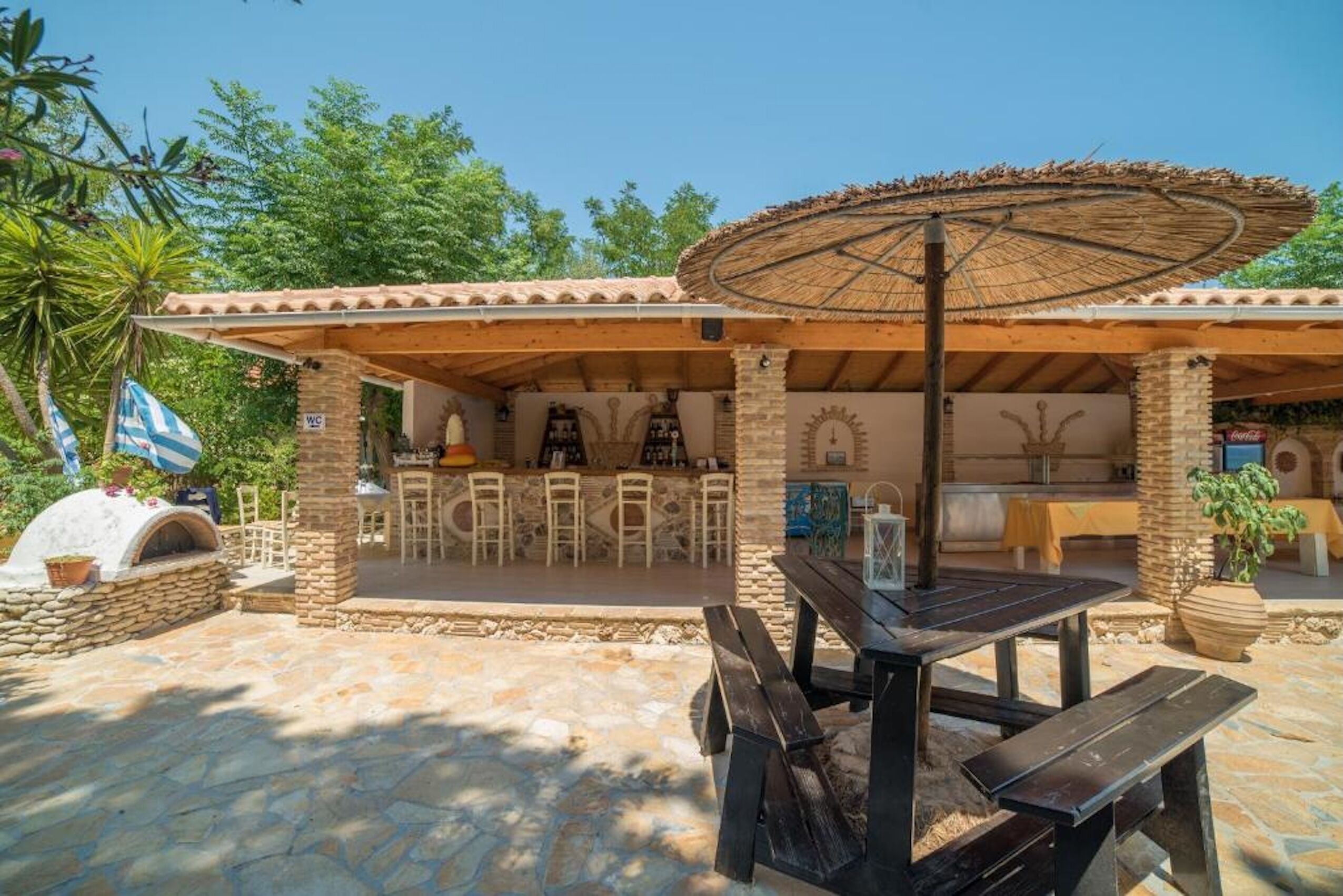 An outdoor patio with stone flooring, a wooden table, and a thatched umbrella.