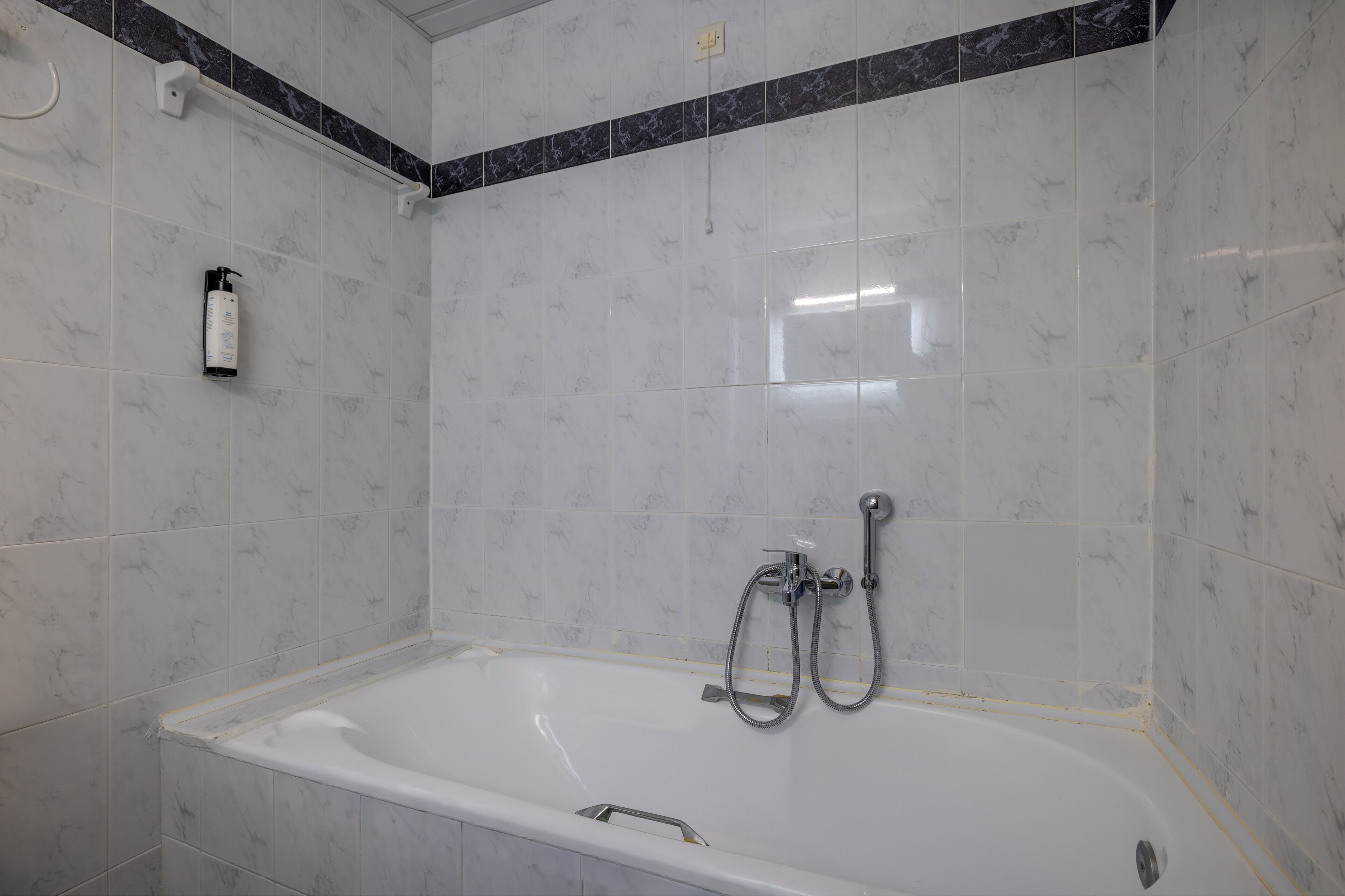 A bathroom with a bathtub, shower, and hand soap dispenser.