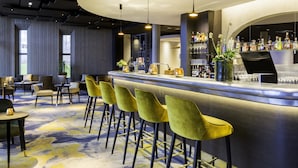Un espace bar moderne avec un comptoir incurvé, des tabourets de bar verts et une variété de bouteilles et de verres exposés sur des étagères.