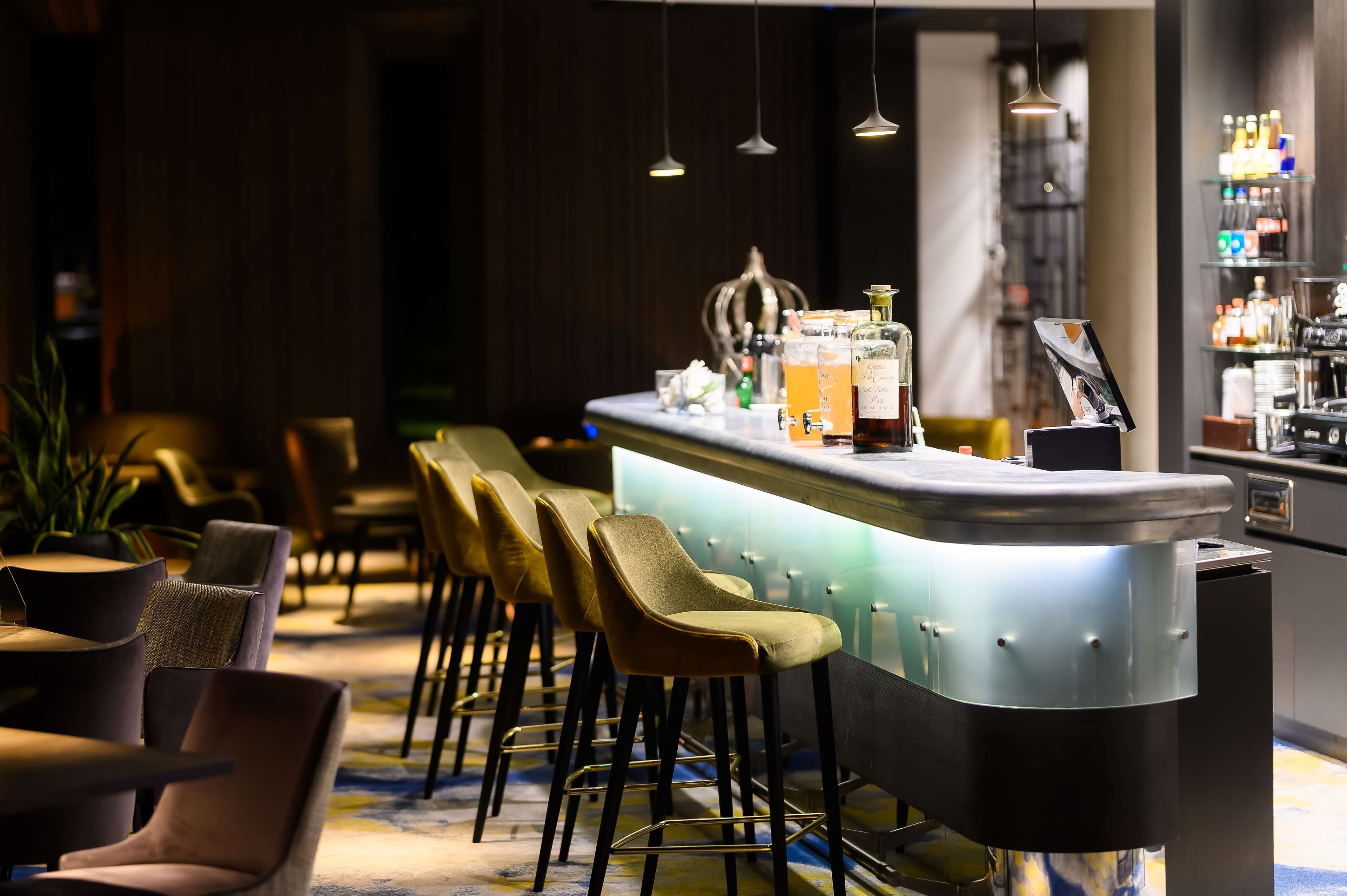 A bar area with a counter, stools, and a shelf with bottles.