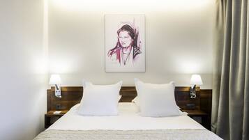 A hotel room with a large bed, two bedside tables with lamps, a headboard, and a framed artwork on the wall.