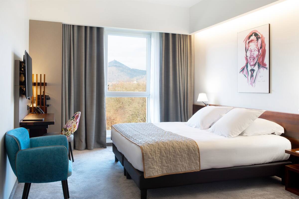 Een hotelkamer met een bed, een bureau, een stoel, een televisie en een raam met gordijnen.