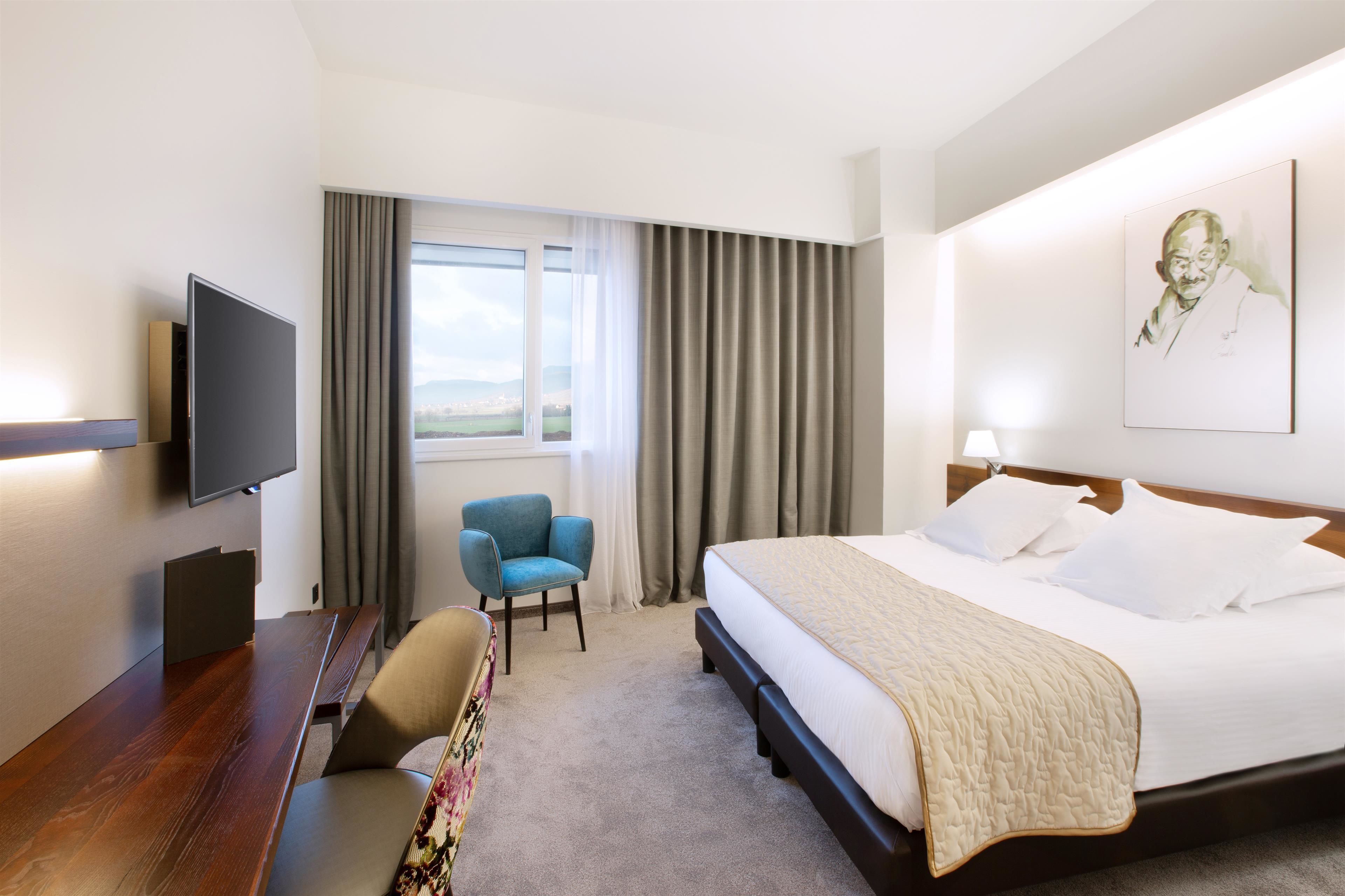 A hotel room with a bed, a desk, a chair, a television, and a window with curtains.
