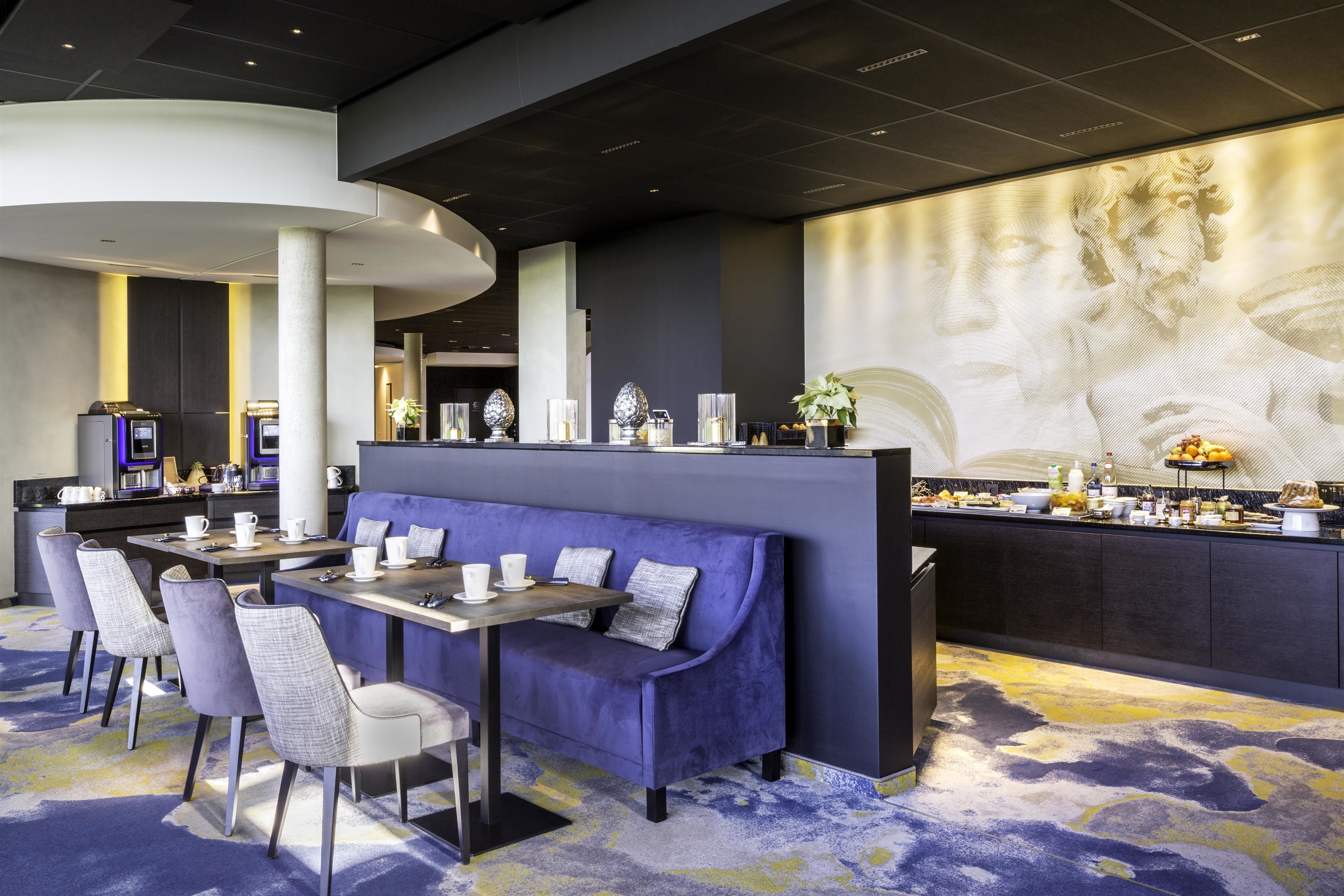 A modern hotel lobby with a seating area, a bar, and a large digital screen displaying a classical artwork.