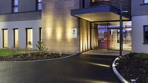 Une entrée moderne avec un passage couvert, une enseigne indiquant un établissement « Best Western Plus » et une porte vitrée donnant accès à l’intérieur.