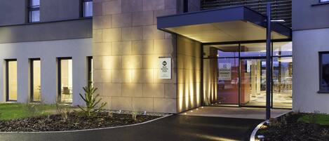 A modern building entrance with a covered walkway, a sign indicating 'Best Western Plus' accommodation, and a glass door leading inside.