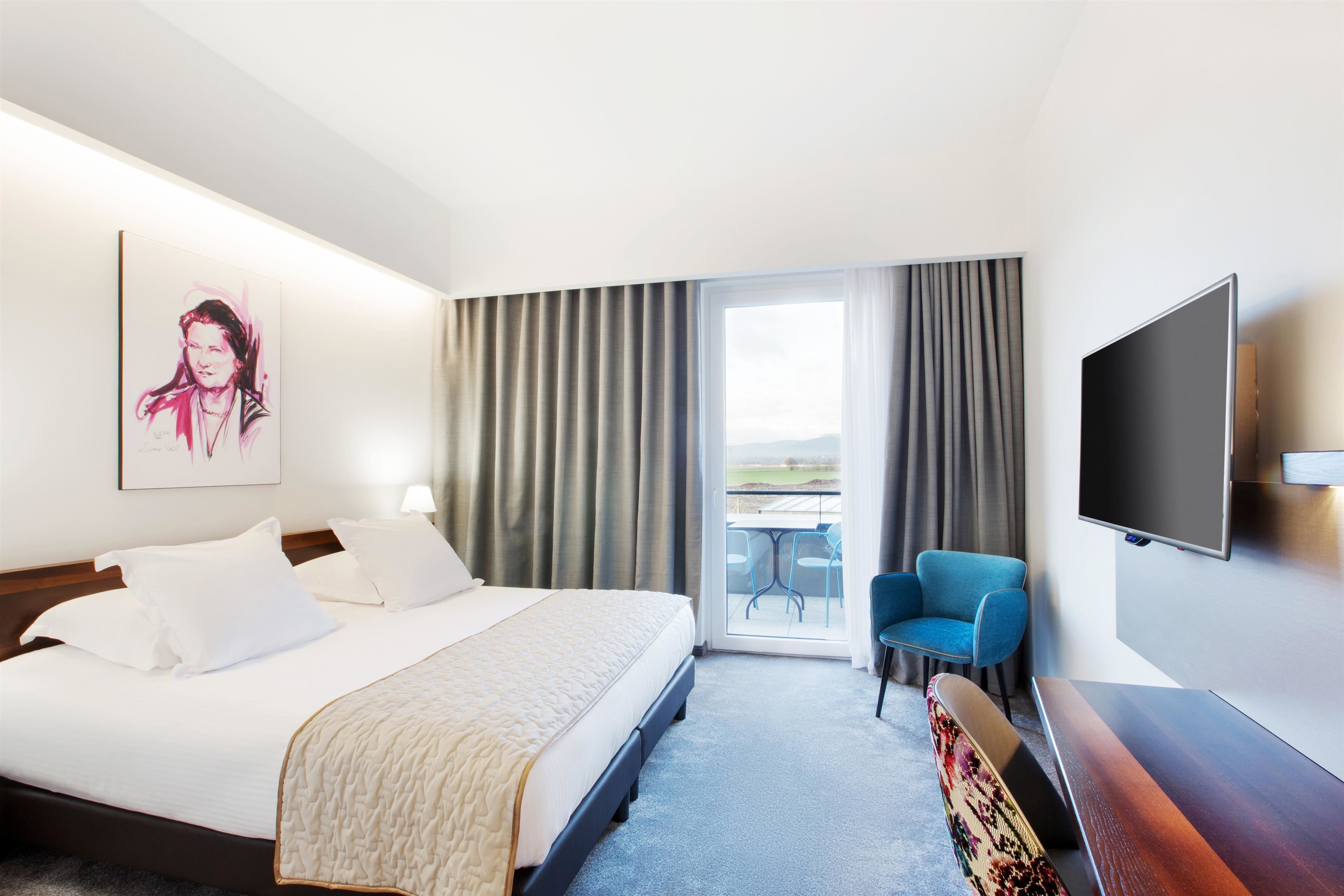 Une chambre d’hôtel comprenant un lit, un téléviseur à écran plat, une chaise et un balcon avec une table et des chaises.