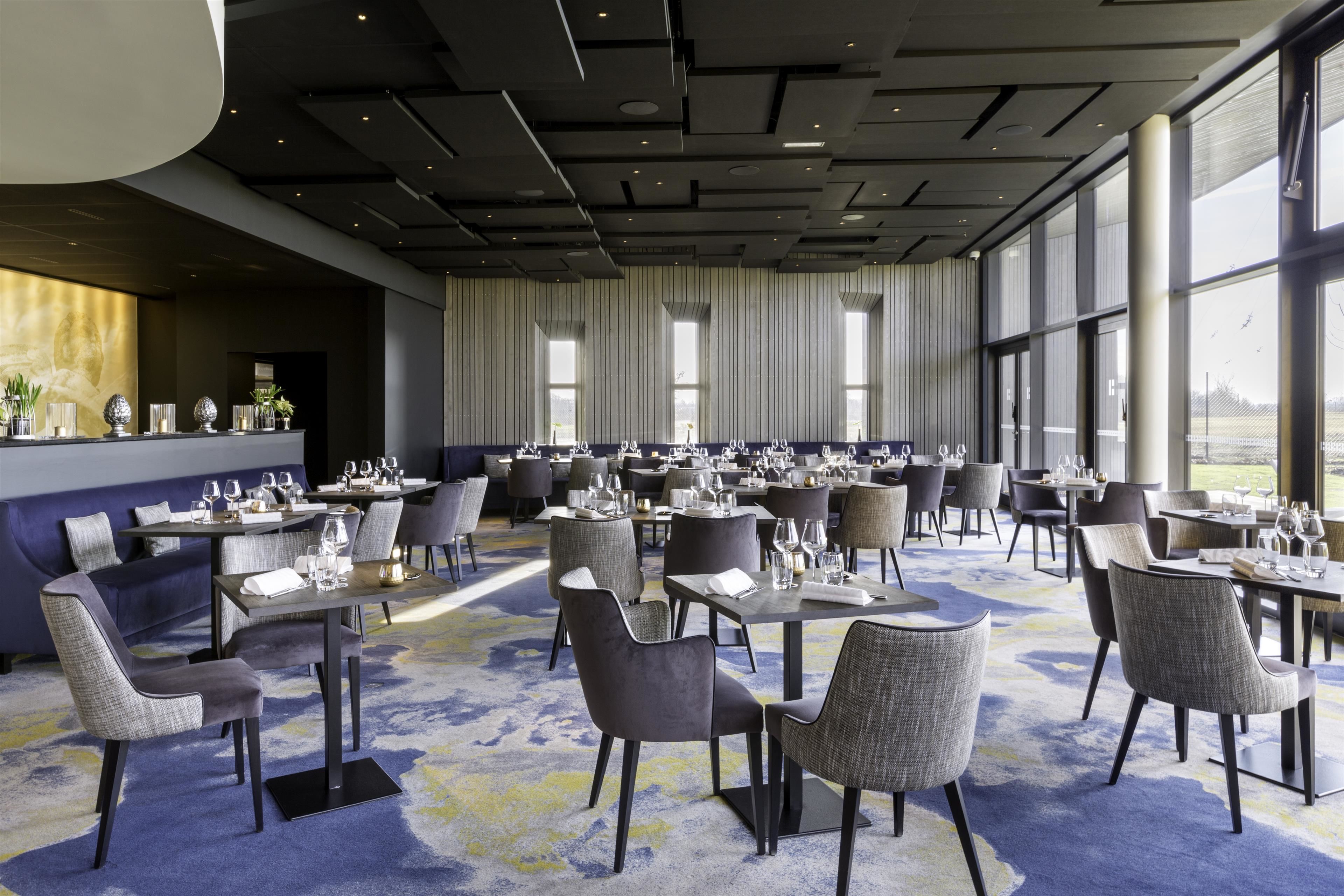 Uma sala de jantar ampla, com várias mesas e cadeiras, grandes janelas e um design de teto moderno.