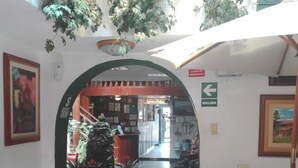 An indoor corridor with a tiled floor, a reception desk, and a sign indicating an exit. - Hostal Santa Apolonia (Cajamarca)