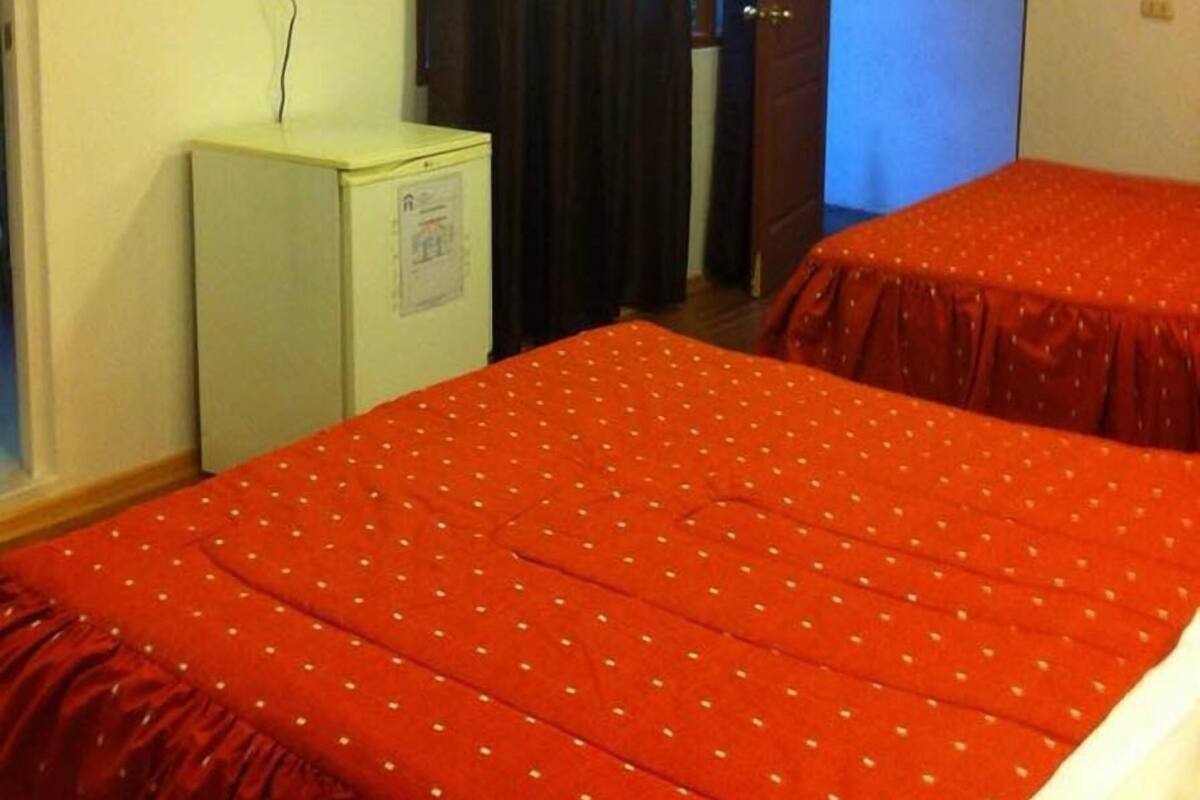Ett hotellrum med två sängar, en tv, ett litet kylskåp och en dörr som leder till ett annat rum.