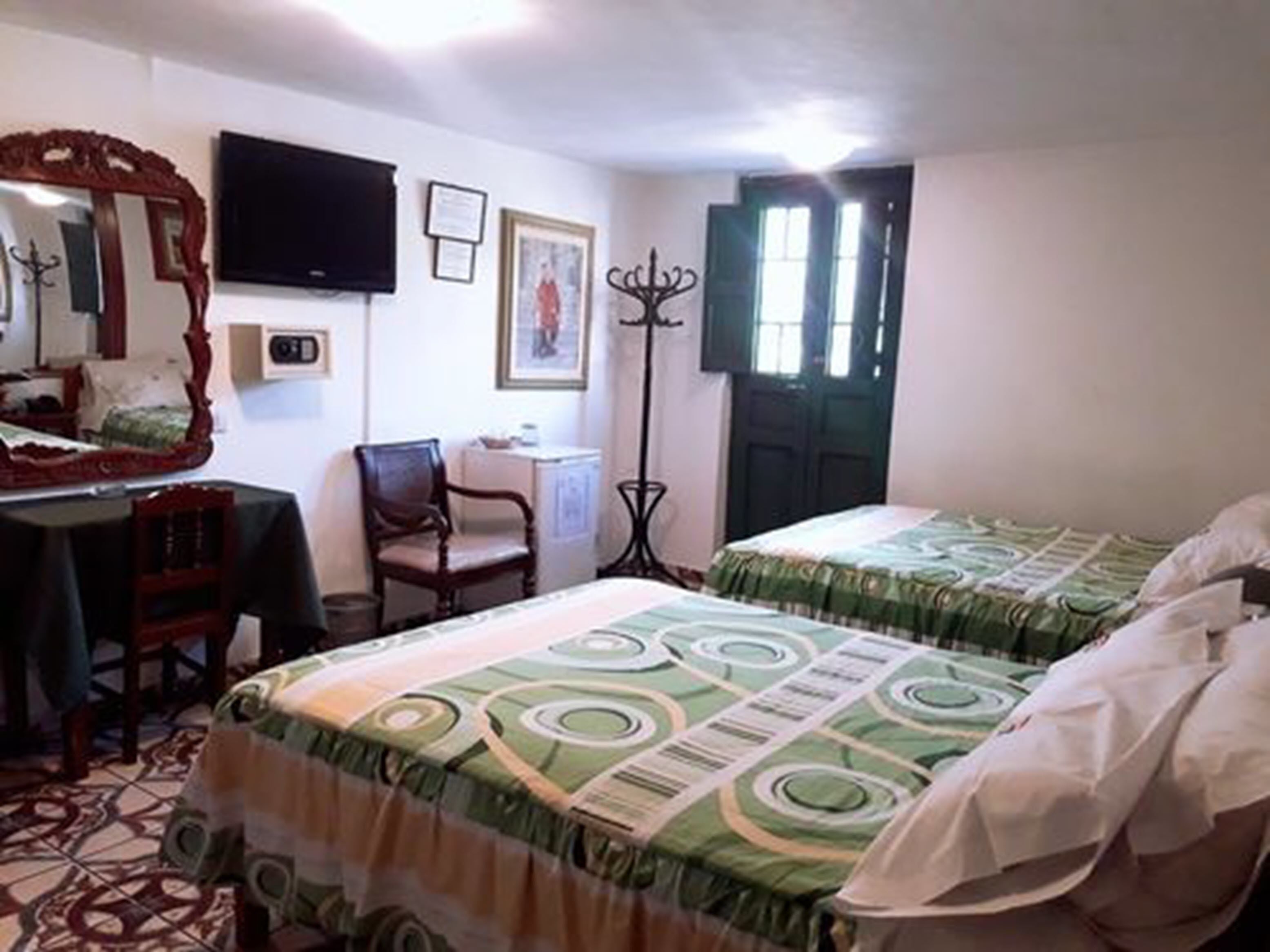 A room with two beds, a desk, a chair, a mirror, a television, and a door with windows.