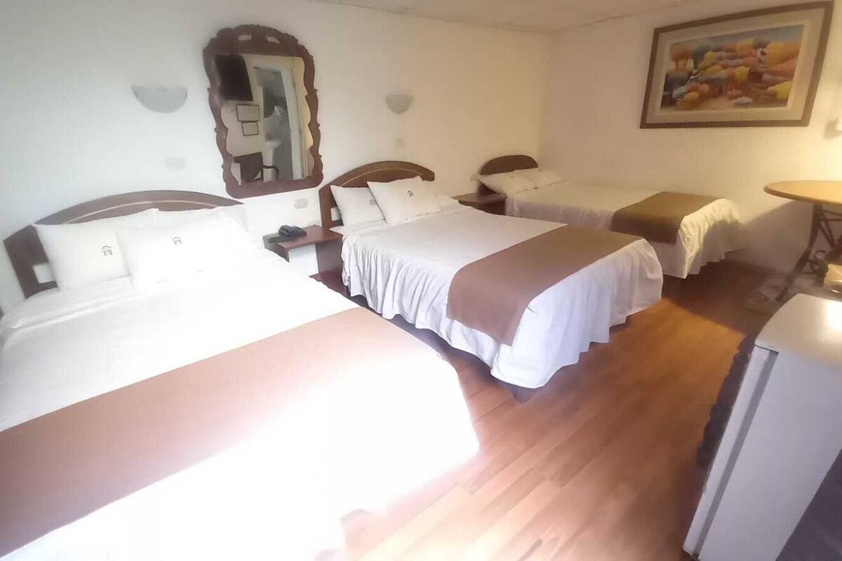 Ett hotellrum med två sängar, ett litet bord, en spegel och en tavla på väggen.